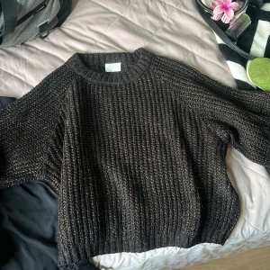 Svart stickad tröja med glittertråd Vila - Mysig svart stickad tröja från Vila med inslag av glittriga trådar i guld och koppar. Tröjan har en ribbad struktur, rund halsringning och långa ärmar. Perfekt för dig som vill ha en enkel men ändå lite extra look.