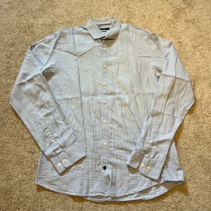 Blåvit rutig skjorta Tiger of Sweden - Snygg blåvit rutig skjorta från Tiger of Sweden i slim fit-modell. Skjortan har klassisk krage, långa ärmar med manschett och knappar framtill. I storlek 39