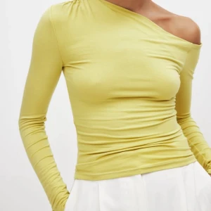 Gul one shoulder topp från NA-KD - Snygg gul långärmad topp från NA-KD med one shoulder-design och lätt rynk vid axeln. Toppens material är mjukt och stretchigt, perfekt för en trendig look. Passformen är tight och färgen är en fräsch ljusgul nyans.