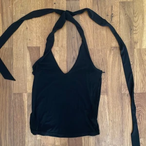Svart halterneck topp från BikBok - Svart halterneck topp från BikBok med djup v-ringning och långa knytband i nacken. Tunt och mjukt material som känns skönt mot huden.