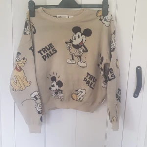 Beige Disney stickad tröja H&M - Beige stickad tröja från H&M x Disney med stora motiv av Musse Pigg, Pluto och Kalle Anka samt texten 'True Pals' över hela tröjan. Långärmad och med rund hals, perfekt för dig som älskar klassiska Disney-karaktärer.