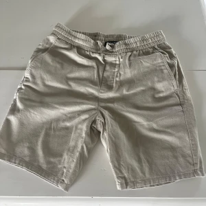 Beige linne shorts  - Snygga beige shorts med elastisk midja och snörning. De har en avslappnad passform och är tillverkade i ett mjukt bomullstyg. Perfekta för varma dagar och enkla att matcha med det mesta. Klassisk design med sidfickor för en chill look.