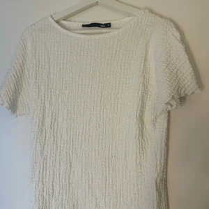 Vit strukturerad t-shirt från 157 - Säljer en vit t-shirt från 157 i storlek XS. T-shirten har en cool strukturerad yta som ger en unik look. Den är kortärmad och har en klassisk rund halsringning. Perfekt för dig som gillar stilrena och trendiga plagg.❤️