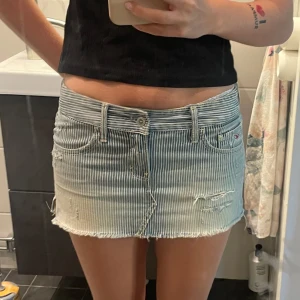 Randig jeanskjol från Hollister - Superfin kort jeanskjol från Hollister med blåvita ränder och slitna detaljer.