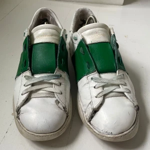 Valentino Open  vit/grön - Välanvända Valentino Garavani Open sneakers i vitt skinn med bred grön läderdetalj över mitten. Perfekta för en sommarsäsong till. 
