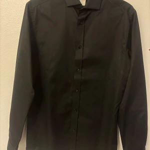 Svart skjorta från Jack & Jones - Stilren svart skjorta från Jack & Jones Premium med klassisk krage och knäppning framtill. Skjortan är tillverkad i 2-ply garn för en mjuk och skön känsla. Perfekt för dig som gillar en enkel och clean look.