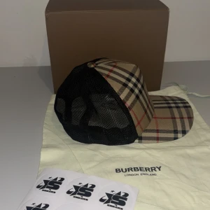 Rutig keps från Burberry - Snygg keps från Burberry med klassiskt rutigt mönster i beige, svart och rött. Kepsen har en justerbar rem baktill och mesh-paneler för ventilation. Perfekt för en stilren look.