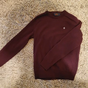 Vinröd tröja från Morris - Säljer en stilren vinröd tröja från Morris i 100% merinoull. Tröjan har en liten broderad detalj på bröstet och långa ärmar. Perfekt för kyligare dagar.