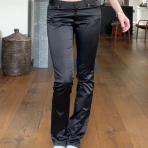 Svarta byxor med bootcut - Snygga svarta byxor med bootcut-stil. De har en låg midja och är tillverkade i ett glansigt material som ger en elegant look. Jag är ca 176 cm lång. Passar mig som bär vanligen 36 i jeans.