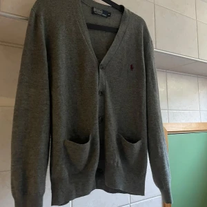 Grå kofta från Polo Ralph Lauren - Säljer en stilren grå kofta från Polo Ralph Lauren med knappar framtill.Den har en broderad logotyp på bröstet.