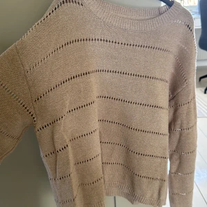 Beige stickad tröja från Noisy May - Säljer en snygg beige stickad tröja från Noisy May. Tröjan har ett diskret hålmönster och ribbade muddar vid ärmslut och nederkant. Perfekt för en stilren look.