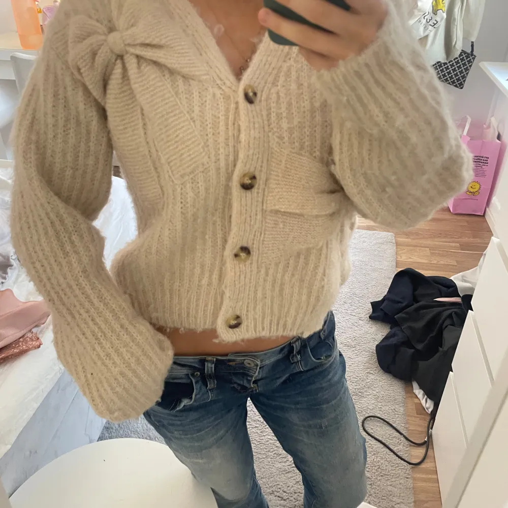 Mysig beige stickad kofta med stora knappar framtill. Koftan har en croppad passform och långa ärmar med ribbade muddar. Perfekt för kyliga dagar!. Neuletakit & Villapaidat.
