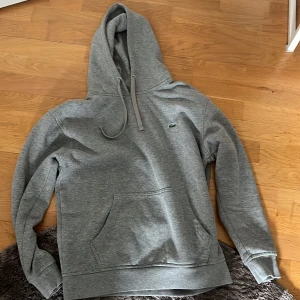 Grå hoodie från Lacoste - Säljer en stilren grå hoodie från Lacoste med klassisk krokodillogga. Storlek S 
