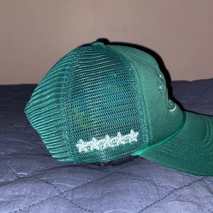 Grön Corteiz keps  - Snygg grön Corteiz keps med broderade stjärnor och ett motiv framtill. Kepsen har ett nätmaterial på sidorna och justerbar rem baktill för perfekt passform. (A-cop)