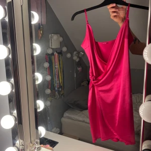 Rosa klänning - Snygg rosa omlottklänning med smala axelband och knytning i midjan. Perfekt för en somrig look med sin ljusa och livfulla färg. Klänningen har en kort längd och är tillverkad i ett mjukt material som ger en fin passform.❤️
