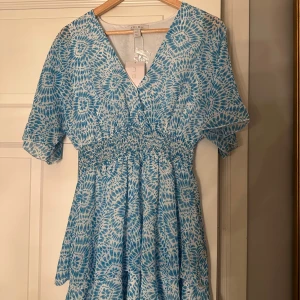 Blåmönstrad klänning  - Säljer en somrig blåmönstrad klänning new Yorker Klänningen har en v-ringad design med korta ärmar och ett elastiskt midjeband som ger en smickrande passform. Perfekt för varma dagar!