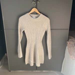 Beige ribbad klänning - Snygg beige ribbad klänning med lång ärm och rund hals. Perfekt för kyligare dagar med sin stickade design. Klänningen har en figurnära passform som framhäver silhuetten.