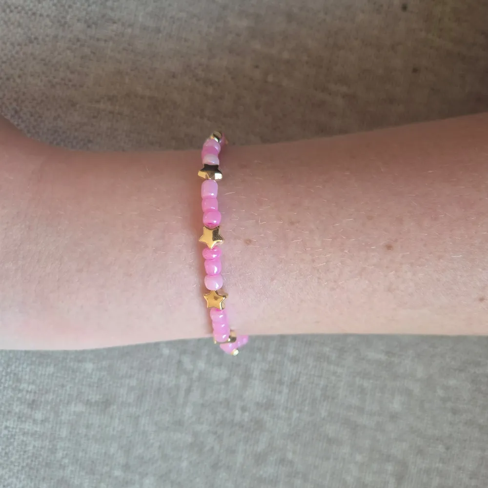 Charmigt armband med rosa pärlor och guldstjärnor. Perfekt för att lägga till en lekfull touch till din stil. Elastiskt band för enkel passform.. Asusteet.