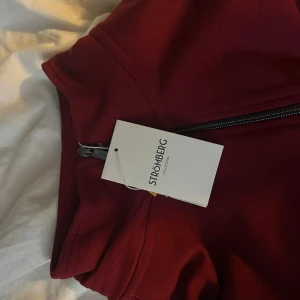 Röd tröja med dragkedja från Strömberg - Snygg röd tröja från Strömberg med halv dragkedja och hög krage. Perfekt för kyligare dagar. Tröjan har långa ärmar och en stilren design som passar till många tillfällen.