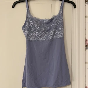 Ljusblå linne med spetsdetaljer - Säljer ett ljusblått linne med vackra spetsdetaljer över bysten. Linnet har smala axelband och en mjuk, bekväm passform. Perfekt för varma dagar eller som ett lager under andra plagg.