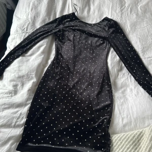 Svart klänning med prickar från H&M - Snygg svart klänning från H&M med glittriga prickar. Den har en tight passform och långa ärmar, perfekt för en kväll ute. Materialet är mjukt och stretchigt, vilket gör den bekväm att bära.öppen rygg OBS No free shipping , går ej att ta bort 