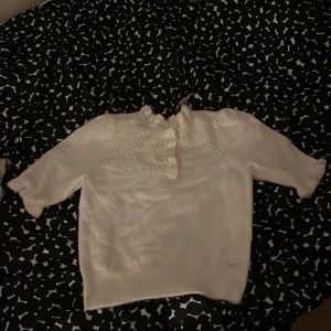 Vit tröja från Holly & Whyte - Säljer en söt vit tröja från Holly & Whyte by Lindex. Tröjan har en fin struktur med knappar framtill och en ribbad krage. Perfekt för en stilren look.