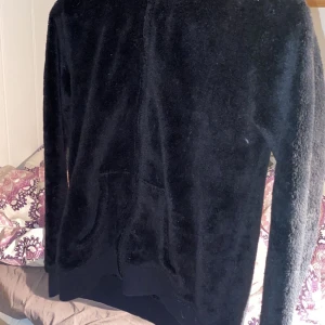 Svart teddyjacka med dragkedja - Mysig svart teddyjacka med dragkedja framtill. Perfekt för kyliga dagar med sin mjuka och fluffiga textur. Jackan har långa ärmar och en bekväm passform.