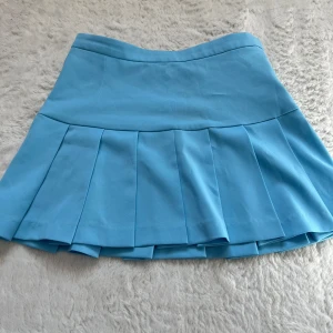 Blå kjol från Weekday - Snygg blå kjol från Weekday med veckad design och dragkedja i sidan. Perfekt för en stilren look. Aldrig använd! Storlek 34 men mer som 36