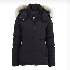 Canada Goose Chelsea Xxs - Säljer en stilren svart dunjacka från Canada Goose med avtagbar huva och pälsdetaljer. Jackan har dragkedja och knappar framtill samt långa ärmar. Perfekt för kalla vinterdagar.