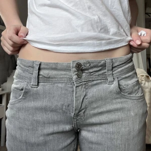 Grå bootcut jeans - Snygga grå bootcut jeans med låg midja och dubbla knappar fram. Perfekta för en avslappnad stil med en touch av retro. Passar bra till både sneakers och klackar.