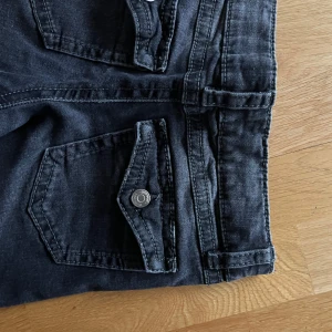 Mörk gråa jeans med knappar på fickan - Mycket bra kvalitet, nästan aldrig använd och säljer pga att de är för små. Inga defekter