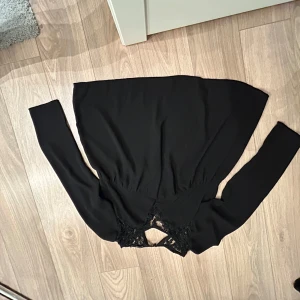 Svart blus från Rut&Circle - Snygg svart blus från Rut&Circle med spetsdetaljer vid halsen. Blusen har långa ärmar och en elegant design som passar perfekt för en stilren look. Perfekt för att lyfta din garderob med något unikt och trendigt. Pris kan diskuteras