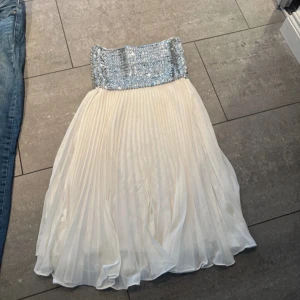 Vit klänning med paljettliv från Elise Ryan - Säljer en elegant vit klänning från Elise Ryan med ett glittrande paljettliv i silver och en plisserad underdel och passar perfekt för speciella tillfällen. 