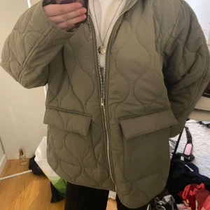 Olivgrön quiltad jacka från H&M - Säljer en olivgrön quiltad jacka från H&M med dragkedja framtill. Jackan har en ribbad krage och stora fickor. Perfekt för våren nu med sin stilrena design och bekväma passform. Storlek XXS men funkar även upp till storlek M