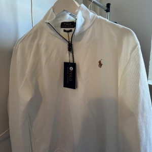 Polo Ralph Lauren Zip - Säljer en stilren zip vit från Ralph Lauren med dragkedja och det klassiska logotypbroderiet på bröstet. Perfekt för en avslappnad och snygg look. Passar bra till både jeans och chinos.