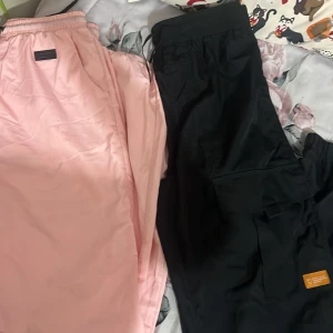 Rosa och svarta byxor - Två par byxor i olika färger. Ett par är ljusrosa och det andra är svart. Båda har elastisk midja och ser bekväma ut för vardagsbruk. Perfekta för en avslappnad stil.