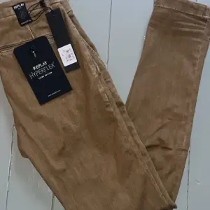 Snygga bruna Replay Hyperflex byxor med en tight passform. Byxorna är tillverkade i ett stretchigt material som ger bra komfort och rörelsefrihet. Perfekta för en stilren look. Jeansen är helt nya aldrig använda och kostar 1800 nya.