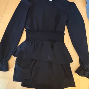 Svart klänning från Gina Tricot - En supersöt volang klänning från Gina Tricot som jag säljer då jag inte använder den längre! Som man ser på bilden har klänningen en liten fläck, men den går nog säkert bort! Klänningen är i storlek 158/164, men passar som XXS/XS.