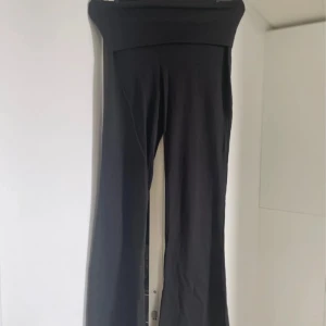 Svarta yogapants från Gina Tricot - Snygga svarta byxor från Gina Tricot med en vik ner midja och utsvängda ben. Säljer då de ej kommer till någon användning.