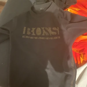 Svart tröja från Boss - Snygg svart tröja från Boss med glittrig logotyp på framsidan. Perfekt för en stilren look. Tröjan har långa ärmar och en klassisk passform.