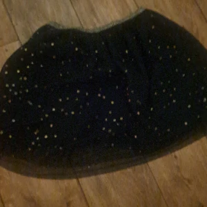 Marinblå glittrig kortkjol med tyll - En marinblå kortkjol med glittriga detaljer i tylltyg. Kjolen har en lätt utsvängd form och är täckt av små glittrande prickar som ger en festlig känsla. Perfekt för dig som vill sticka ut med en cool look.