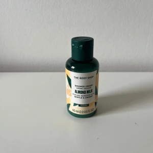 The Body Shop Almond Milk Shower Cream - En liten, grön plastflaska med duschkräm från The Body Shop. Doft av mandelmjölk, passar känslig och torr hud. Vegansk och krämig formula, 60 ml. 