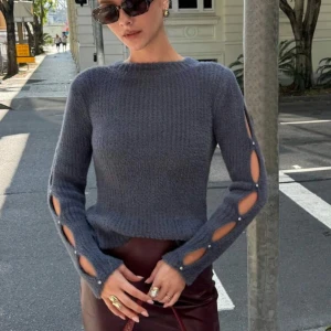 Grå stickad tröja med kristalldetaljer - Säljer en supermjuk och fluffig grå stickad tröja med långa ärmar. Ärmarna har coola öppna slitsar längs hela armen, dekorerade med små kristaller. Perfekt för dig som vill ha något unikt och trendigt i garderoben! Använd endast en gång