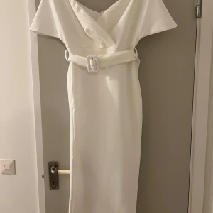 Vit offshoulder långklänning med bälte - Vit midiklänning med offshoulder-skärning och breda ärmar. Klänningen har tajt midja med matchande bälte och slits bak. En väldigt elegant klänning, använd bara en gång.