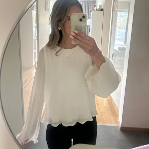 Vit blus med volangkant  - Säljer en söt vit blus med ribbad struktur och volangkant längst ner. Blusen har långa, vida ärmar som ger en flowy känsla och rund halsringning. Perfekt att styla med smycken och jeans för en chill look.