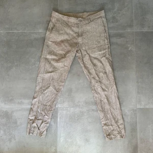 Beige tapered byxor Massimo Dutti - Snygga beige byxor från Massimo Dutti i tapered fit. Tillverkade i en mix av polyester och bomull, med klassisk design, bälteshällor och fickor både fram och bak. Perfekta för en clean och stilren look. 