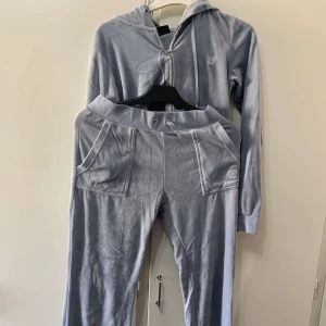 Ljusblå mjukisbyxor med snörning - Säljer ett par ljusblå mjukisbyxor i mjukt fleecematerial med bred resår och snörning i midjan. Byxorna har stora fickor framtill och en broderad logga på ena benet. Perfekta för chill dagar eller när du vill vara extra bekväm.