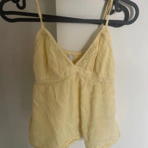 Ljusgul linnetopp med spetsdetaljer - Supersöt ljusgul linnetopp med tunna axelband och v-ringning. Toppen har fina spetsdetaljer.Storlek S frn networker och sitter jätte fint.