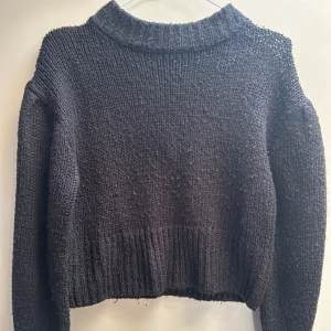 Svart stickad tröja med hög krage - Mysig svart stickad tröja med hög ribbad krage och långa ärmar. Tröjan har en loose passform och bred ribb vid nederkant och ärmslut. Perfekt för kyliga dagar och enkel att matcha med jeans eller kjol.