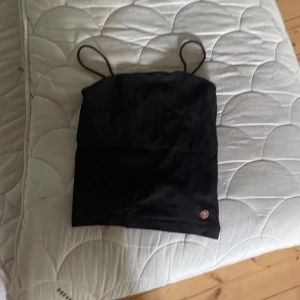 Svart linnetopp med smala axelband - Enkel och stilren svart linnetopp med tunna axelband och en liten smiley-detalj längst ner. 